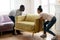 African couple placing new modern armchair in light living room