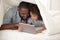 African father and daughter with tablet computer hiding under blanket