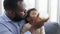 African father Sitting on sofa, holding and feeding newborn baby from bottle milk in living room. Authentic lifestyle candid real