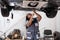 African female auto mechanic fixing car, mechanic repairing car on lift in garage