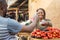 african girl selling tomatoes in a local african market to a male customer smiling and feeling happy and satisfied