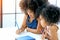 African girls as older and younger sister write or draw something on white paper near the book in front of glass windows with day