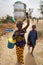 African kids walking in the countryside, a young girl is carrying kitchenware on her head