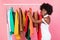 African Lady Picking Clothes Posing Near Clothing Rail, Pink Background
