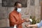 African male receptionist wearing medical mask using infrared thermometer for measuring body temperature of office