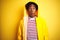 African man with afro hair wearing rain coat with hood standing over isolated yellow background afraid and shocked with surprise