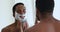 African man applying shaving foam on face looking in mirror