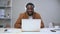 African man with beard in headphones behind laptop greets and waves hand Spbas.