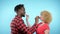 African man Caucasian woman eating black and white marshmallows. blue background