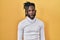 African man with dreadlocks wearing turtleneck sweater over yellow background making fish face with lips, crazy and comical