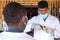 African man in full protective medical gear from coronavirus using an infrared thermometer to test a man in front of a business