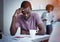 African man sitting at kitchen, reading bank notification, his wife standing with bills