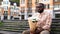 African man sitting lonely on city bench, holding flower bouquet, failed date