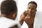 African Man Touching Acne Pimple On Face Standing In Bathroom