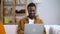 African man working at home on computer on background of interior.