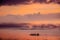 African Men pushing along with long poles a Dhow canoe in an orange sunset on the Indian Ocean near Mombasa, Kenya