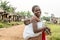 African mother with cute baby in sling in beautiful street of village with straw huts.