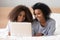 African mother lying on bed with teen daughter browsing internet