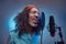 African Rastafarian singer male wearing a blue shirt and beanie emotionally writing song in the recording studio.