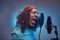 African Rastafarian singer male wearing a blue shirt and beanie emotionally writing song in the recording studio.