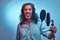 African Rastafarian singer male wearing a blue shirt and beanie emotionally writing song in the recording studio.