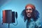 African Rastafarian singer male wearing a blue shirt and beanie emotionally writing song in the recording studio.