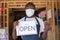 African small business owner wearing a face mask and holding an open sign in front of his shop gestures for people to come in