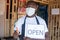 African small business owner wearing a face mask and holding an open sign in front of his shop and gives a thumbs up