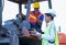 African technician worker woman use laptop to discuss with her team who stay on tractor in cargo container shipping area