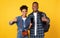 African Travelers Couple Showing Smartphone Screen Gesturing Thumbs-Up, Yellow Background