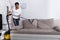 African Woman Cleaning Sofa With Vacuum Cleaner