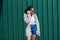 African woman with dreads hair, in jeans shorts  posed against green steel wall