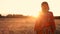 African woman farmer in traditional clothes standing in a field of crops, wheat or barley, in Africa at sunset or sunrise