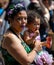 African woman with a flower wreath on her head and a baby on her hands walking in the crowd on the street, New York, USA