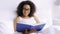 African woman reading book in bed at home bedroom