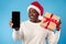 African Woman Showing Smartphone Screen Holding Christmas Gift, Blue Background