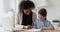 African woman tutor helping caucasian child with homework at home