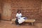 African woman in a white T-shirt holding a baby in her arms and sitting on a bench near a clay hut