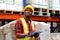 African worker wearing safety vest and helmet, holding file folder document at warehouse factory. Male logistics staff checking