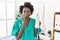 African young physiotherapist woman holding massage body lotion covering mouth with hand, shocked and afraid for mistake