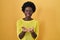 African young woman standing over yellow studio smiling with hands palms together receiving or giving gesture