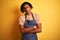 Afro american barista man with dreadlocks wearing apron over isolated yellow background skeptic and nervous, disapproving