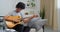 Afro american boy teenager male musician black man artist sitting on sofa at home tuning guitar string tone sounding