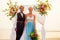 Afro american female in the role of the groom and short blonde haired bride in blue dress in ceremony under wedding arch