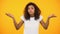 Afro-american female shrugging shoulders, unsure of choice, yellow background