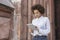 Afro american girl stands on the street near the building and works on a tablet