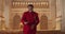 Afro american male performer in red suit looking to camera and singing while standing at row of wooden pews in hall