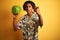 Afro american man with dreadlocks holding watermelon over isolated yellow background annoyed and frustrated shouting with anger,