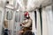 Afro-American passenger man in red hat stand in subway train, using mobile phone, listens to music with wireless headphones in