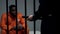 Afro-american prisoner in cell looking at jail guard with baton, harassment